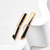 Close-up of gold-plated S925 earrings with a two-part angular design and sleek black enamel inlay, laid against a sculptural white ceramic background to highlight their bold, clean-lined structure.