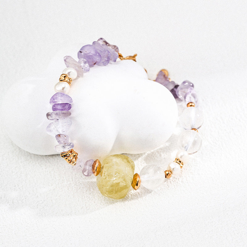 A vibrant amethyst and crystal bead bracelet with a large yellow stone centerpiece and golden spacers, elegantly coiled on a smooth white surface, showcasing its natural asymmetry and minimalist elegance.