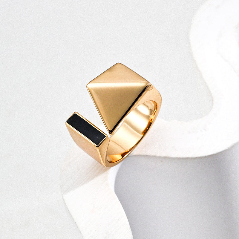 Close-up of a gold-plated S925 silver open ring with one side featuring a smooth pyramid and the other set with sleek black enamel, placed on sculptural white props to emphasize its architectural geometry and high-shine polish.