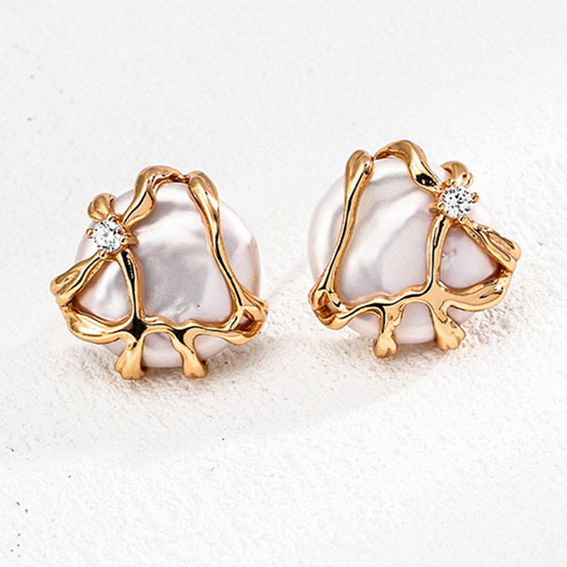 Close-up of two natural pearl earrings encased in abstract gold sculpted 925 silver, each adorned with a brilliant zircon for added sparkle.