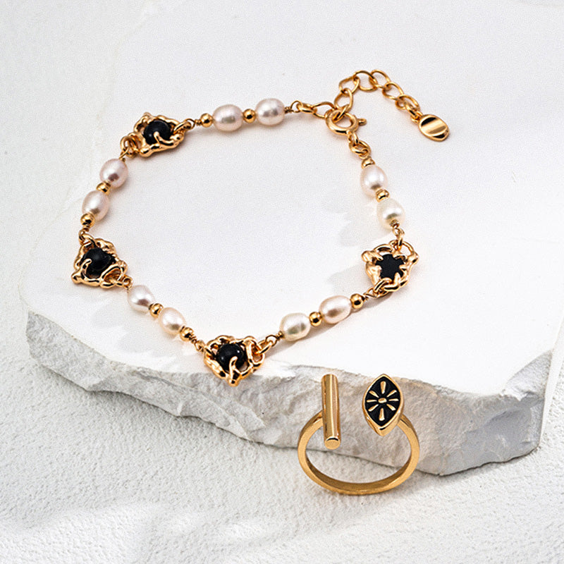 Artistic composition of a handcrafted bracelet with freshwater pearls and black onyx stones set in gold-plated 925 silver, paired with a minimalist gold ring on a white stone platform.