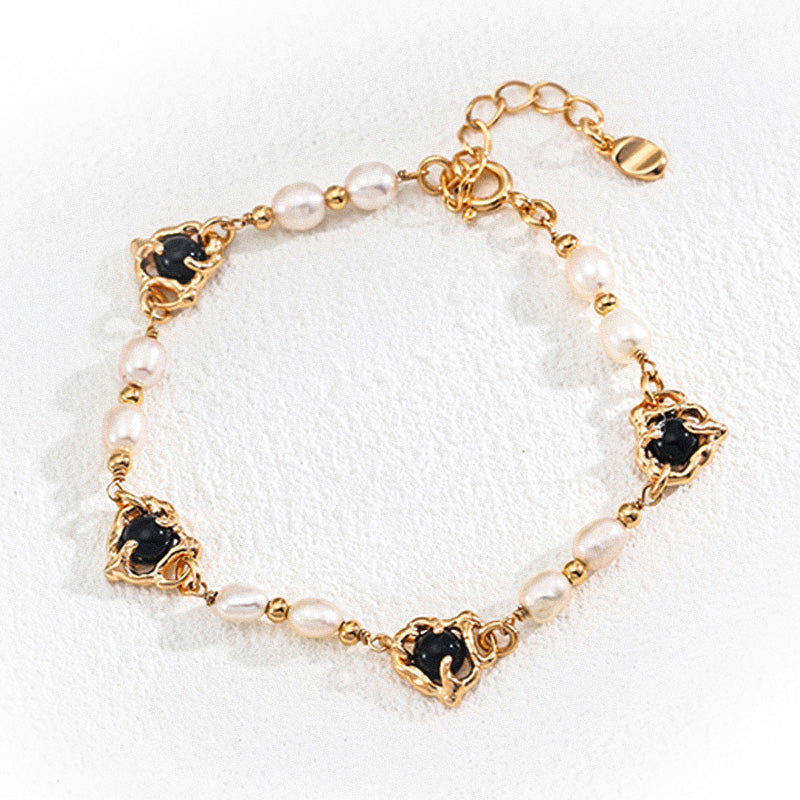 Delicate vintage bracelet made of 925 silver, adorned with irregular white pearls and black onyx stones framed in baroque-inspired gold settings, styled on a clean textured background.