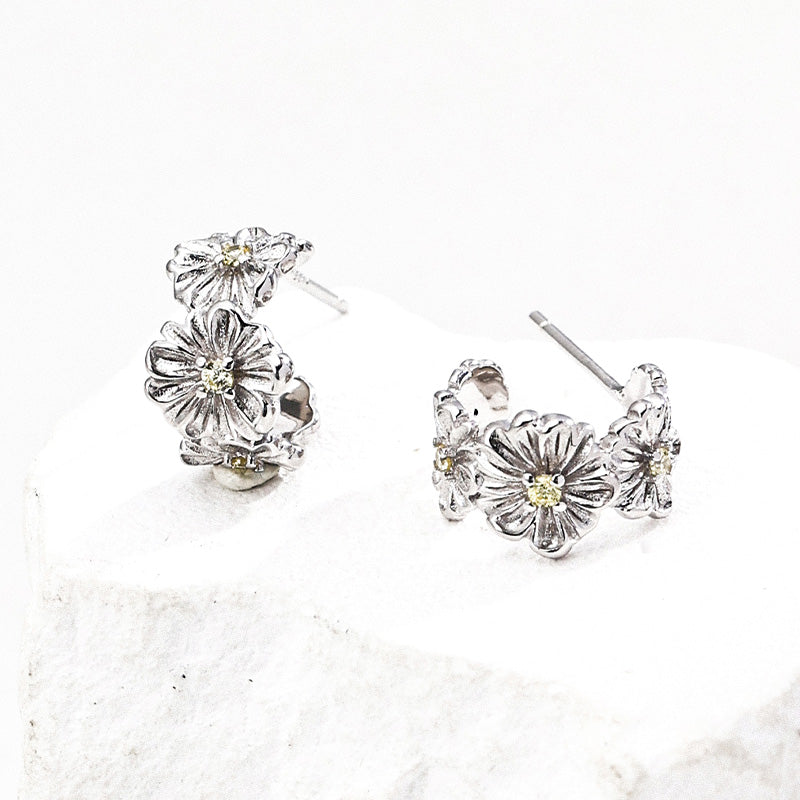 Detailed image of S925 sterling silver floral stud earrings, each bloom adorned with sparkling yellow zircon, placed on a textured white display.