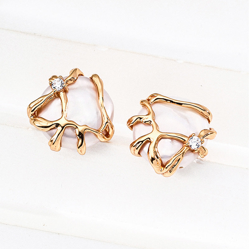 A pair of handcrafted earrings featuring baroque natural pearls wrapped in a flowing, sculpted 925 silver gold-tone setting with zircon accents.