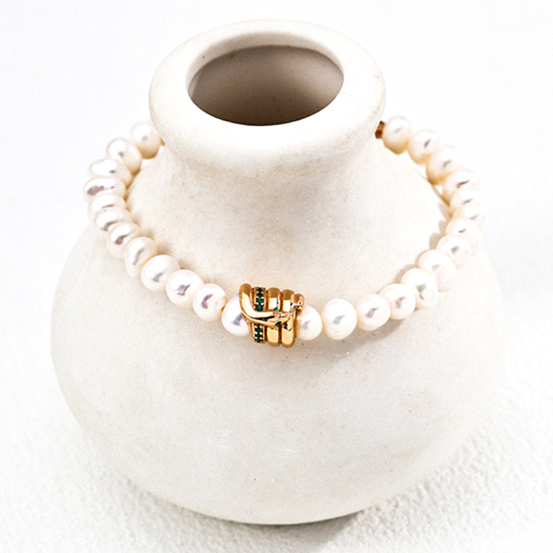 Natural freshwater pearl bracelet featuring a unique gold and green zircon buckle centerpiece, displayed on a ceramic vase.