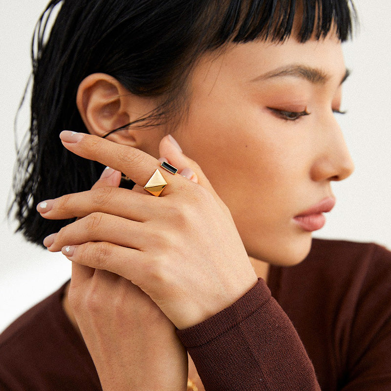 A model wearing the gold-tone S925 silver geometric enamel ring on her index finger, showing its bold contrast between glossy black enamel and minimalistic pyramid structure, exuding modern edge.