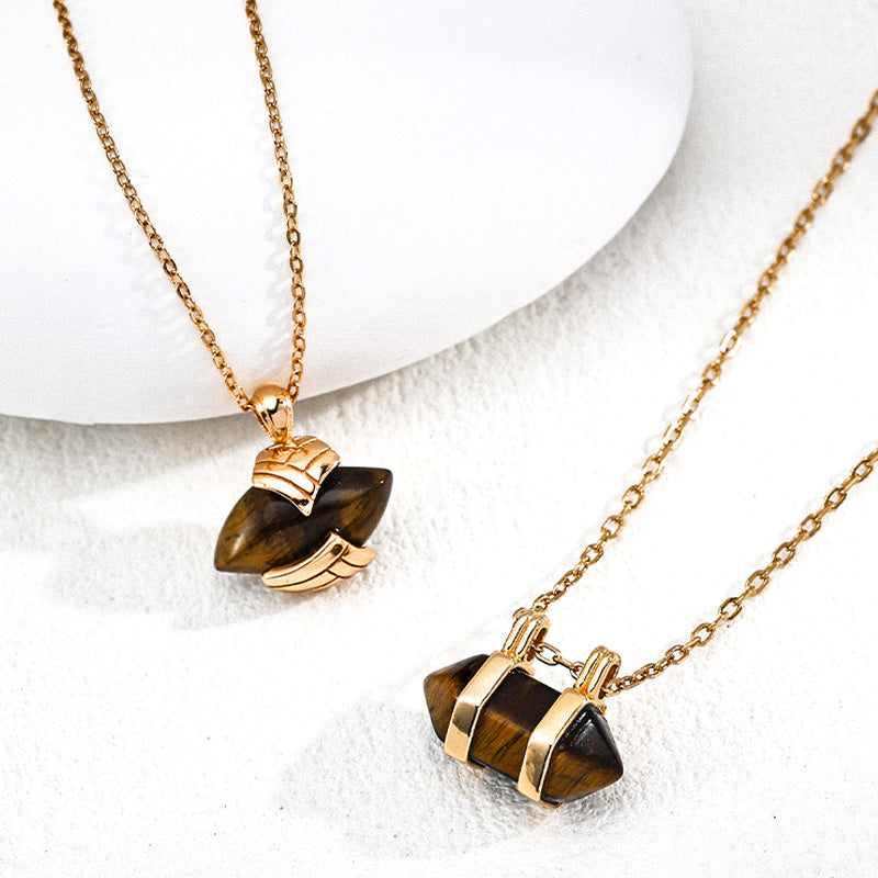 Two S925 silver necklaces with tiger's eye stone pendants, one with wing-inspired gold detailing and the other with minimalist double-bar design, side by side on white stone.