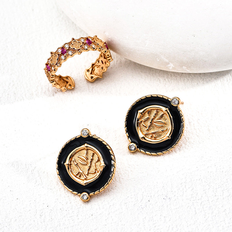The gold-tone S925 zircon ring displayed next to round medallion-style earrings in black enamel and gold.