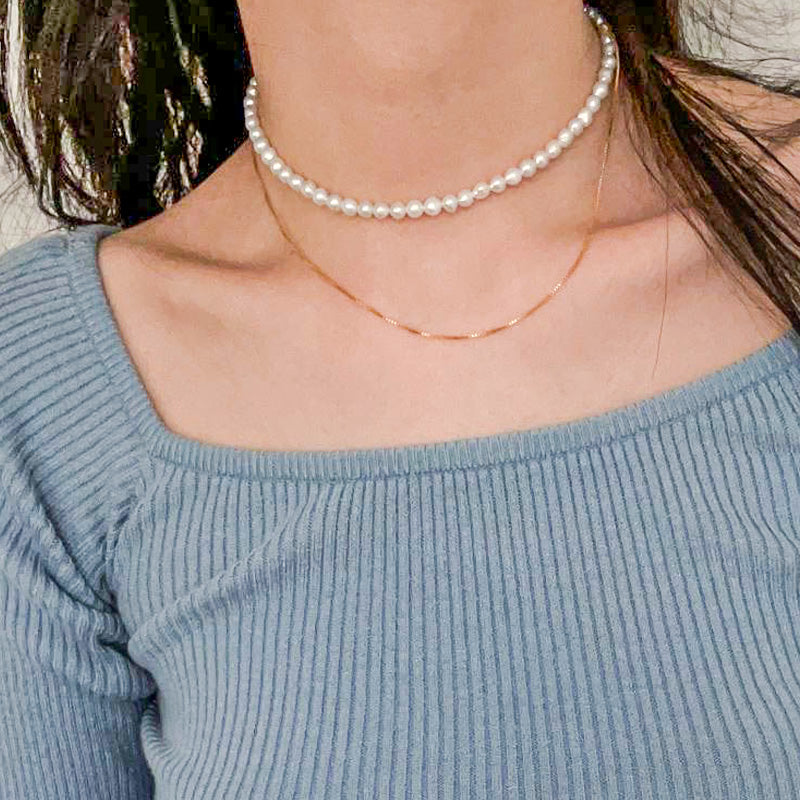 Minimalist two-layer pearl and gold chain necklace worn as a choker, offering a fresh take on classic pearl styling.