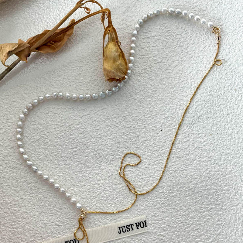 Flat lay of a double-strand pearl necklace with a contrasting gold chain, styled with dried floral elements for a soft, timeless aesthetic.