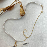 Flat lay of a double-strand pearl necklace with a contrasting gold chain, styled with dried floral elements for a soft, timeless aesthetic.