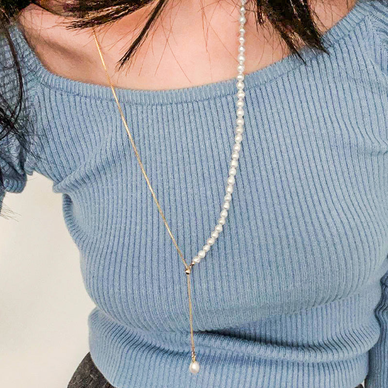 Asymmetrical freshwater pearl necklace with a long drop pendant detail, gracefully layered over a ribbed blue top.