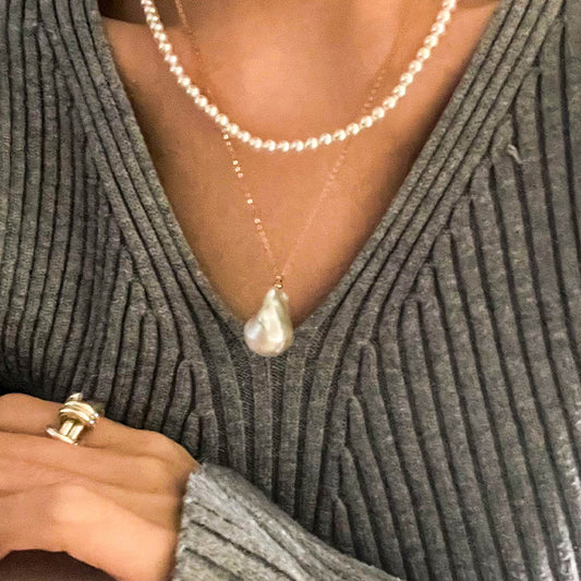 Close-up of a 14K gold necklace with a large white baroque pearl pendant, styled over a ribbed knit top.