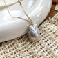 Natural white baroque pearl pendant on a fine 14K gold chain, styled on a ceramic plate and woven fabric.