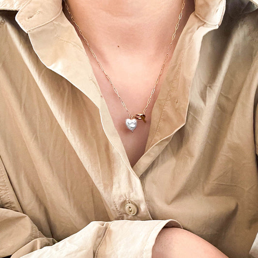 Close-up of a woman wearing a 14K gold heart-shaped baroque pearl necklace with an OT clasp, styled with a beige shirt.