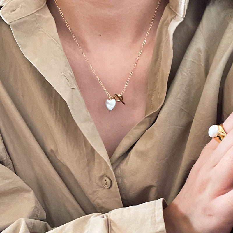 Minimalist styling of a heart-shaped pearl necklace with 14K gold toggle clasp, worn with a neutral-toned shirt.