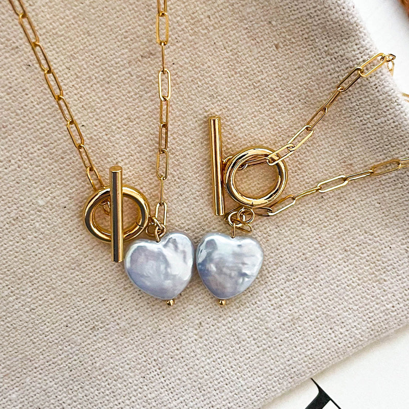 Matching set of white baroque heart pearl necklaces with bold 14K gold toggle clasps, laid on canvas for product styling.