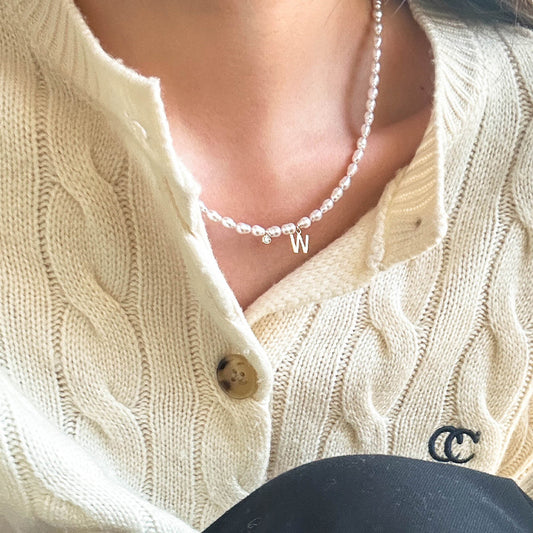 Model wearing a delicate freshwater pearl necklace with 18K gold 'W' charm, styled over a soft knit sweater