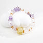 A vibrant amethyst and crystal bead bracelet with a large yellow stone centerpiece and golden spacers, elegantly coiled on a smooth white surface, showcasing its natural asymmetry and minimalist elegance.