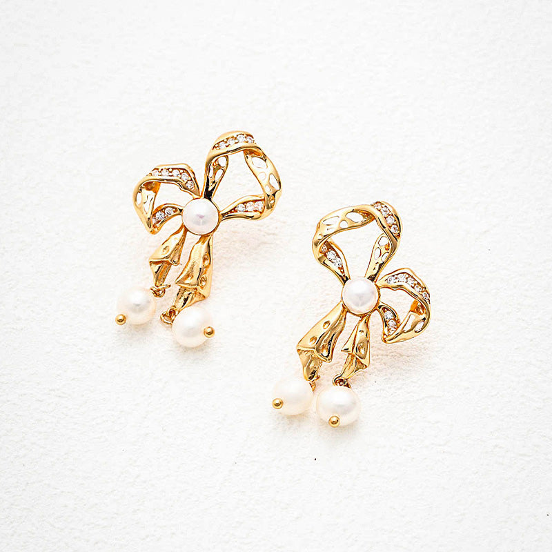 Dainty gold ribbon bow earrings featuring sparkling accents and dangling freshwater pearls, perfect for adding a touch of romance and refinement.