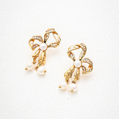 Dainty gold ribbon bow earrings featuring sparkling accents and dangling freshwater pearls, perfect for adding a touch of romance and refinement.
