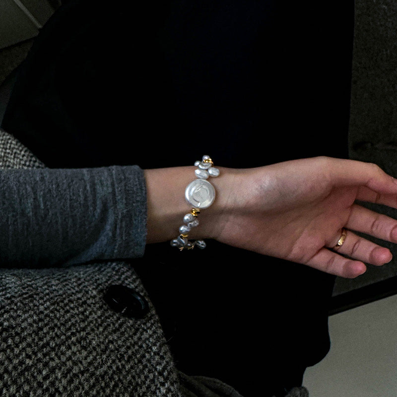 Close-up of a woman's wrist wearing a keshi baroque pearl bracelet with gold accents, styled with a dark knit blazer.