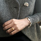 Elegant styling of a baroque pearl and gold bracelet on a woman's wrist, paired with a statement pearl ring and textured grey outfit.