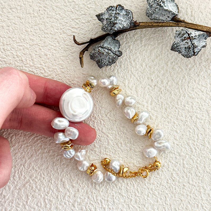 Hand holding a keshi baroque pearl bracelet with organic white pearls and 18K gold-plated elements, styled with a botanical accent.