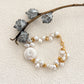 Styled composition of a baroque pearl bracelet with gold details, arranged beside a dried botanical branch on textured ivory background.