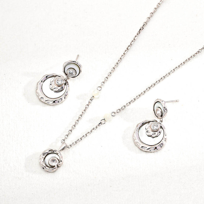 Flatlay of white gold tone necklace and earrings in 925 silver, featuring mother-of-pearl and zircon — sculpted elegance in soft light.