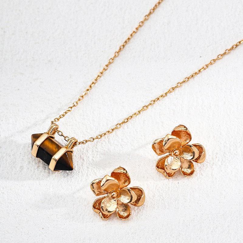 The tiger’s eye pendant necklace is displayed alongside a pair of textured gold flower earrings, arranged on a neutral surface to highlight their warm tones and natural charm.