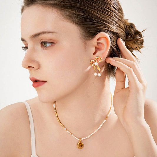 Chic portrait of a model wearing sparkling gold bow pearl earrings and a luminous freshwater pearl necklace with a tiger's eye pendant, blending romantic sophistication with artistic charm.