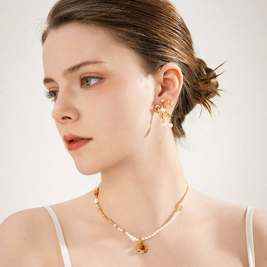 Elegant model showcasing gold ribbon bow earrings adorned with pearls, paired with a delicate freshwater pearl necklace featuring a warm tiger's eye pendant, embodying timeless grace and natural beauty.