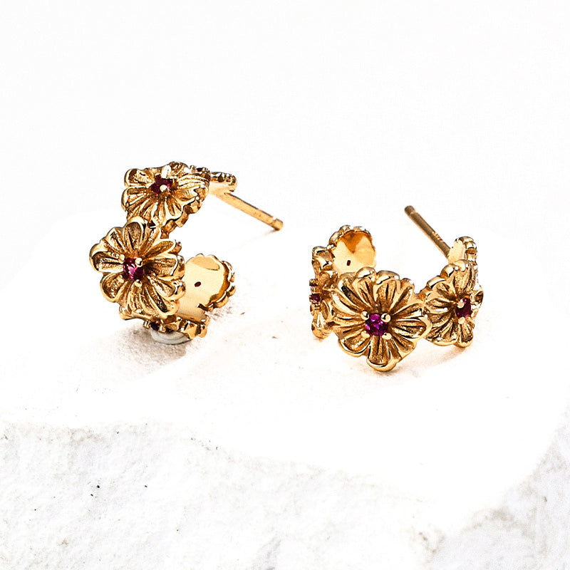 Close-up of S925 silver gold-tone floral earrings featuring intricate flower carvings with red zircon centers, styled on a white stone background.