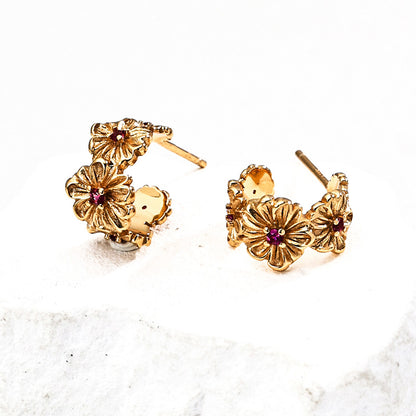 Close-up of S925 silver gold-tone floral earrings featuring intricate flower carvings with red zircon centers, styled on a white stone background.