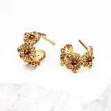 Close-up of S925 silver gold-tone floral earrings featuring intricate flower carvings with red zircon centers, styled on a white stone background.