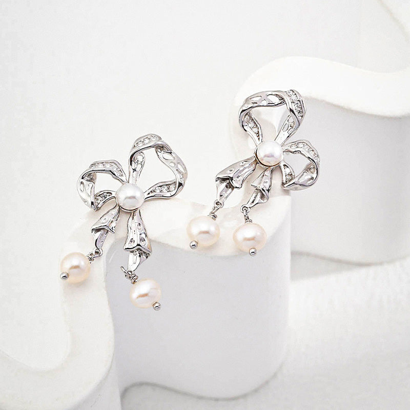 Charming silver ribbon bow earrings with luminous freshwater pearls, offering a graceful, vintage-inspired elegance.