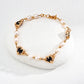 A close-up of a vintage-style bracelet crafted in S925 silver, featuring alternating natural pearls and black onyx stones with ornate gold-toned floral settings, laid on a smooth white stone.