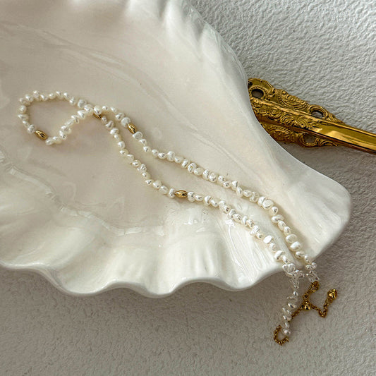 White mini freshwater pearl necklace resting on a seashell-shaped dish with gold elements – simple, radiant, and warm-toned