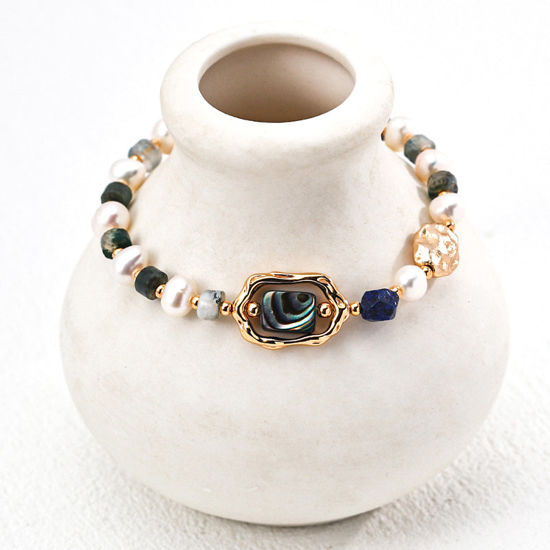 Artistic close-up of a S925 silver bracelet draped on a ceramic vase — designed with natural pearls, lapis lazuli, and a shimmering abalone shell centerpiece.